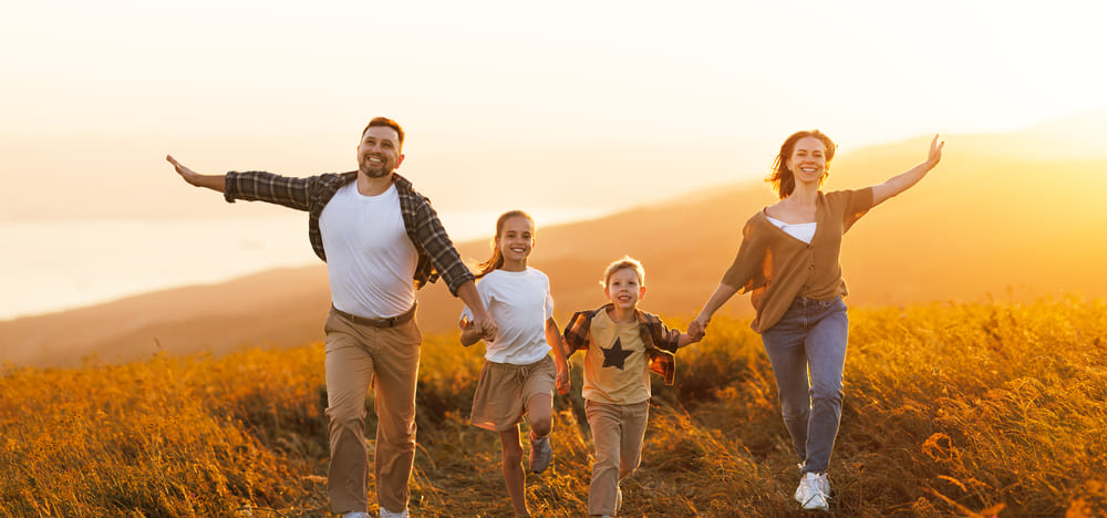 Eine glückliche Familie mit Eltern, Mann, Frau und zwei Kindern, die Hand in Hand über ein Feld laufen