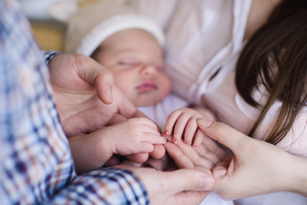 Mutter, Vater und Neugeborenes halten gegenseitig die Hände